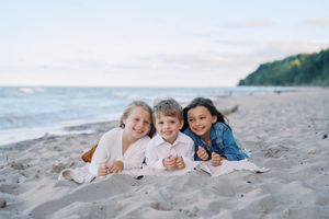 Family members lying together on sandy beach during sunset photo session.