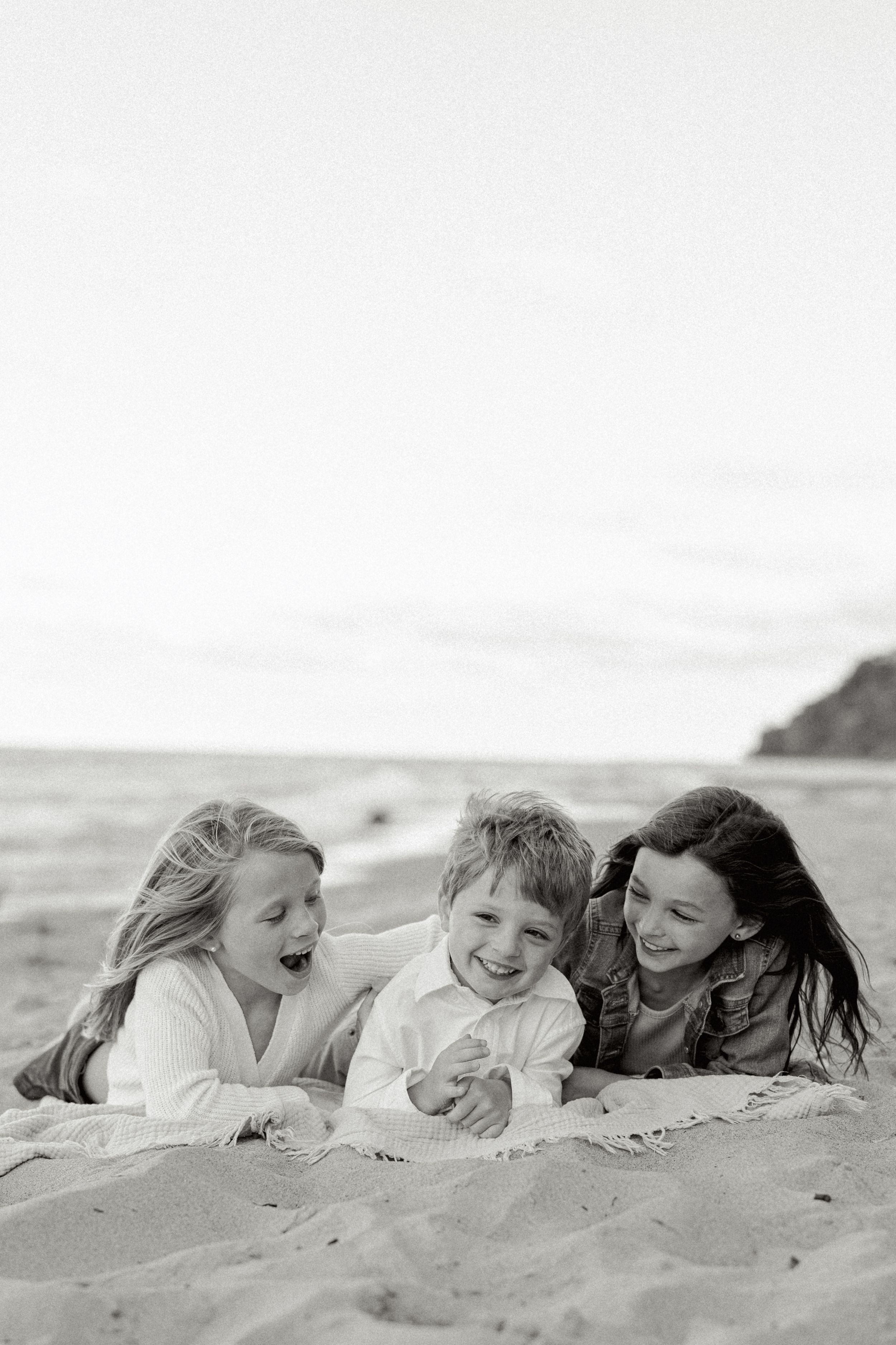 Black and white image series captures joyful friends lying together on sandy beach.