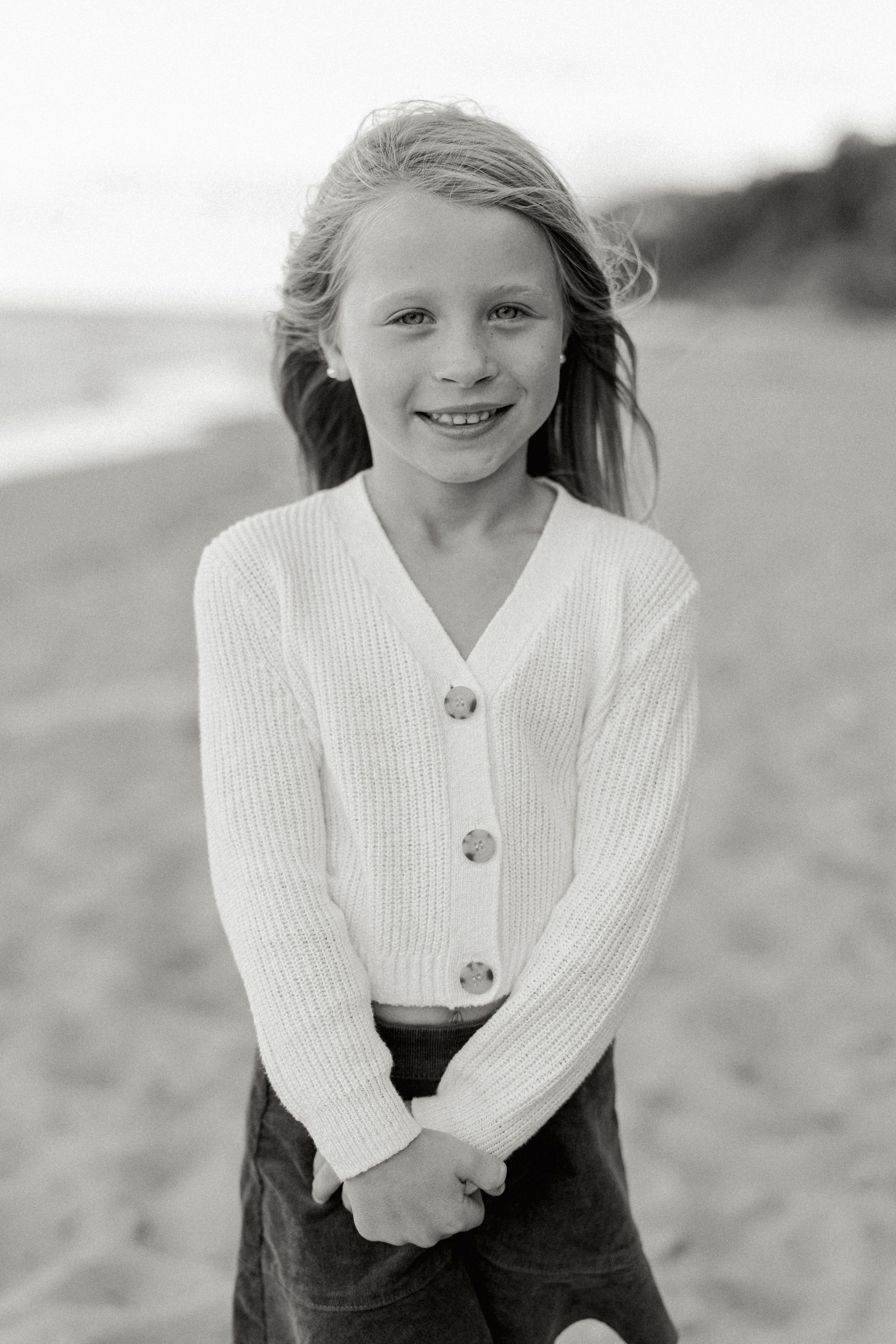A series of four black and white photos showing someone in a white sweater and dark pants on a beach.