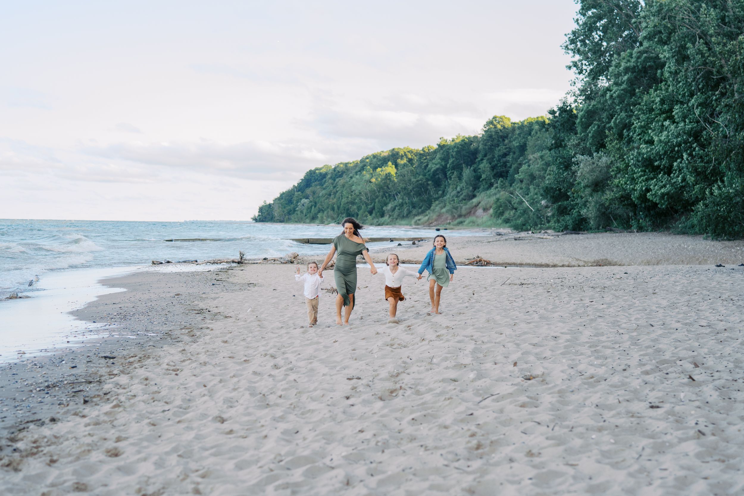 People walking along a scenic beach shoreline with lush green trees and vegetation in the background.