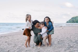 Family enjoying a playful moment together on a sandy beach during sunset with ocean waves in the background.