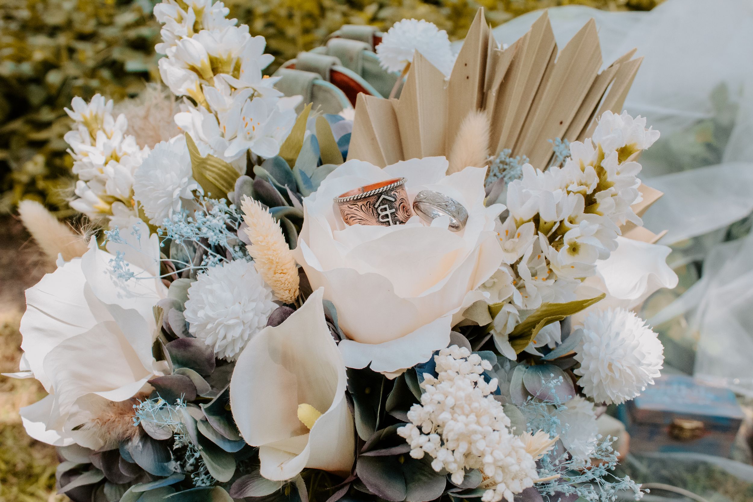 Elegant wedding bouquet with white roses, calla lilies, and rings nestled among soft blooms and dried grasses.