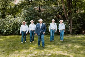 Groom and groomsmen in cowboy hats and jeans pose outdoors on green grass at a rustic country wedding.