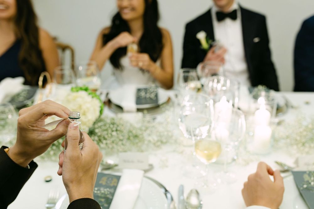 Guest opening small bottle during Swedish snaps toast tradition at wedding dinner in Lisbon