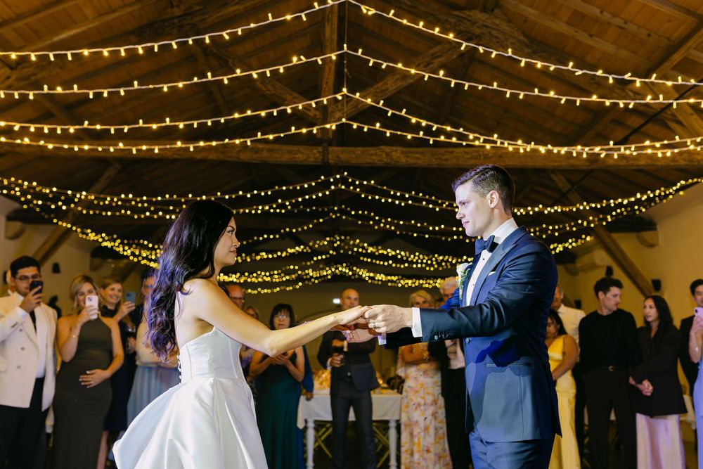 Bride and groom holding hands during first dance surrounded by guests under fairy lights in Lisbon