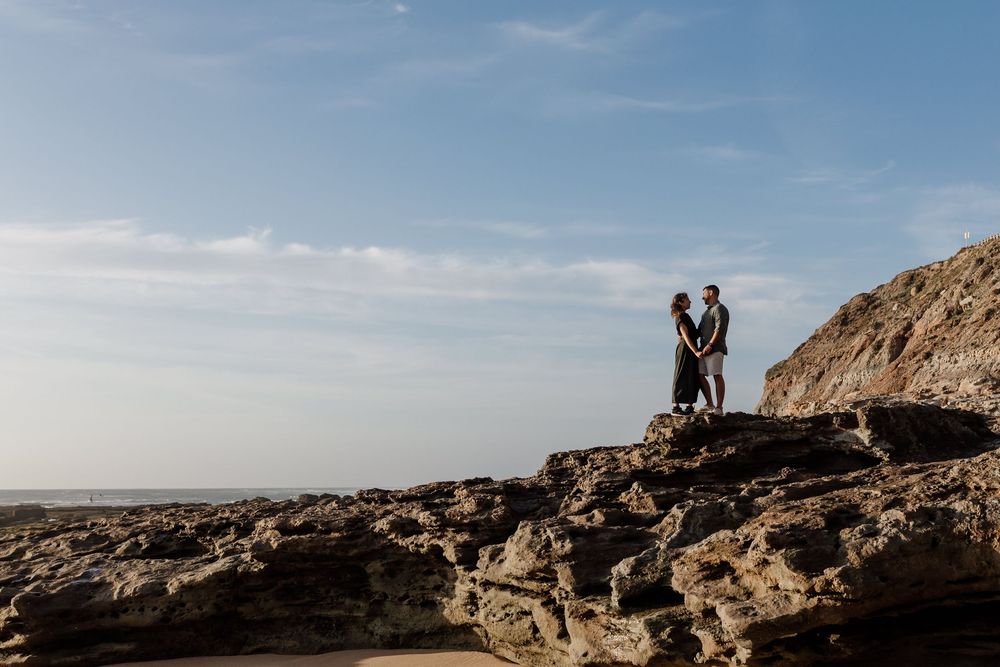 Two people standing on a rocky hill overlooking a scenic landscape.