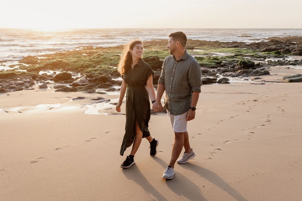 A young couple walking together on a sandy beach at sunset.