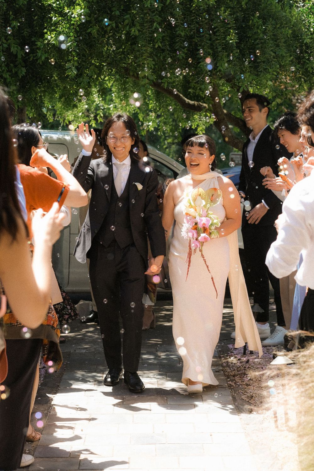 Two brides walk hand-in-hand through a joyful bubble send-off after their outdoor wedding ceremony.