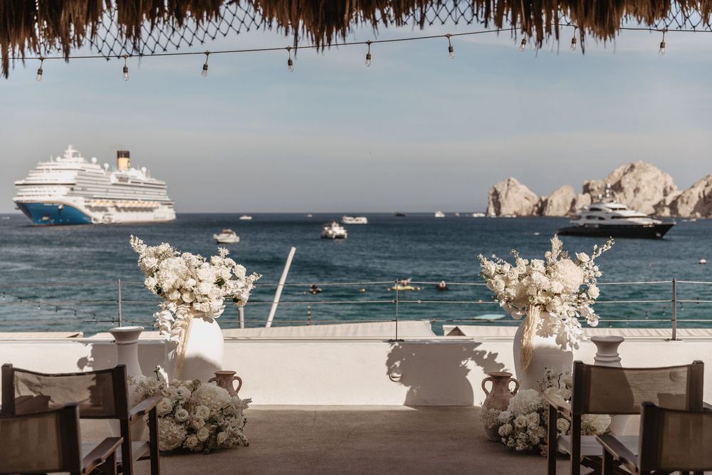 Luxury yacht and elegant wedding decor with white floral arrangements along the ocean coastline at sunset.