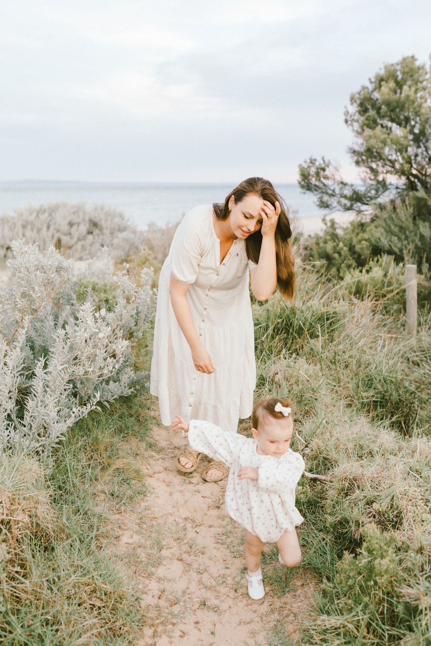 A person in a flowing white dress walks through a field of wild sage and desert brush on a sunny afternoon.