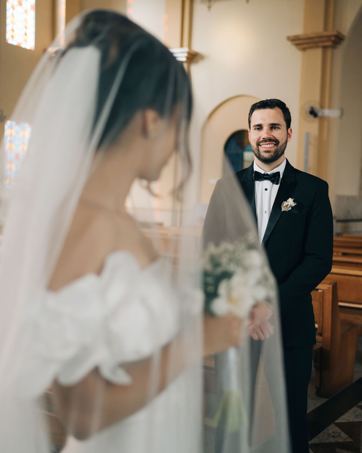 noiva com véu e buquê durante cerimonia de casamento na igreja com noivo ao fundo