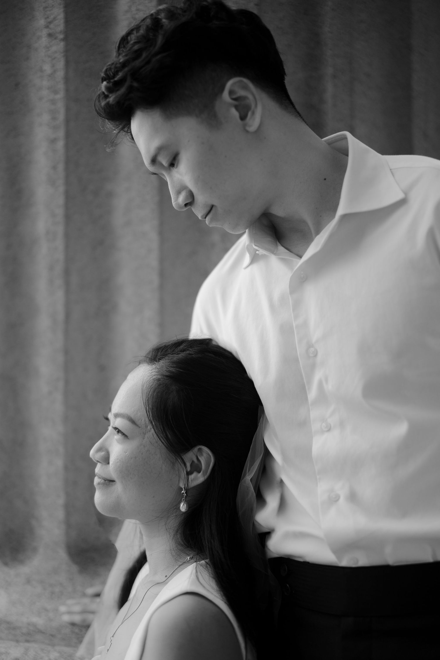 Black and white portrait of Asian couple, man standing behind seated woman in profile.