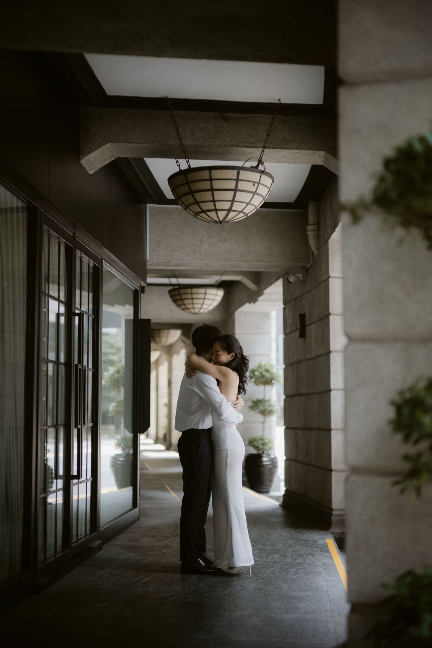 Bride and groom sharing romantic kiss in dimly lit hotel corridor with hanging lantern.
