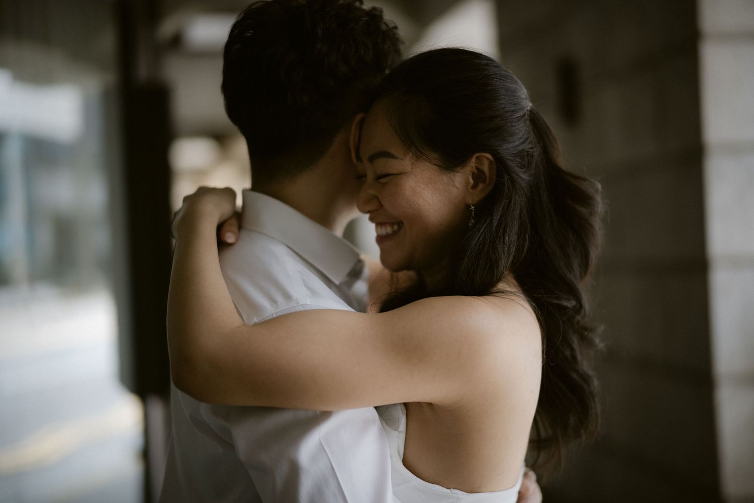Joyful bride laughing while embracing groom outdoors during wedding photo session.