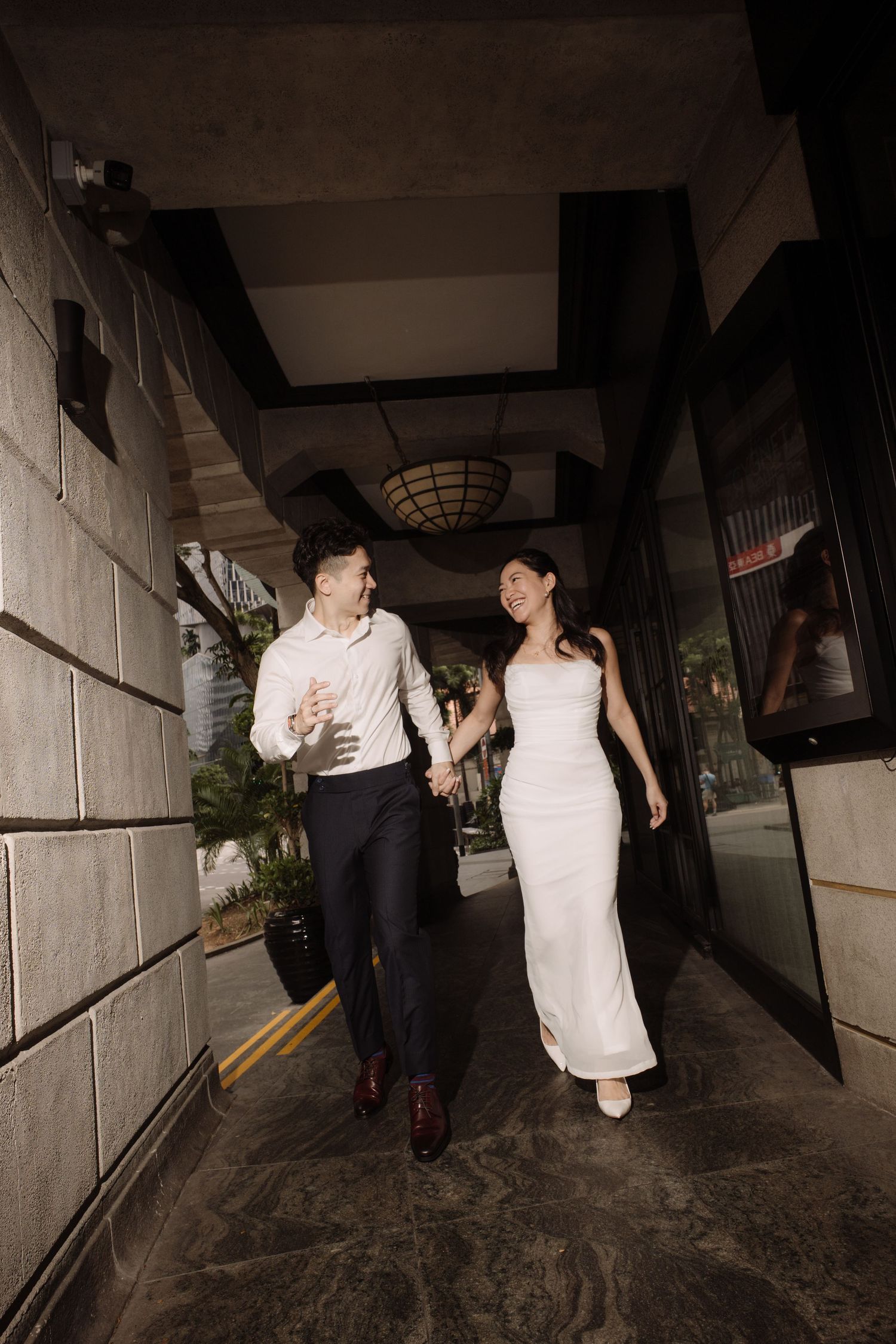 Happy couple holding hands and walking through elegant covered walkway in wedding attire.