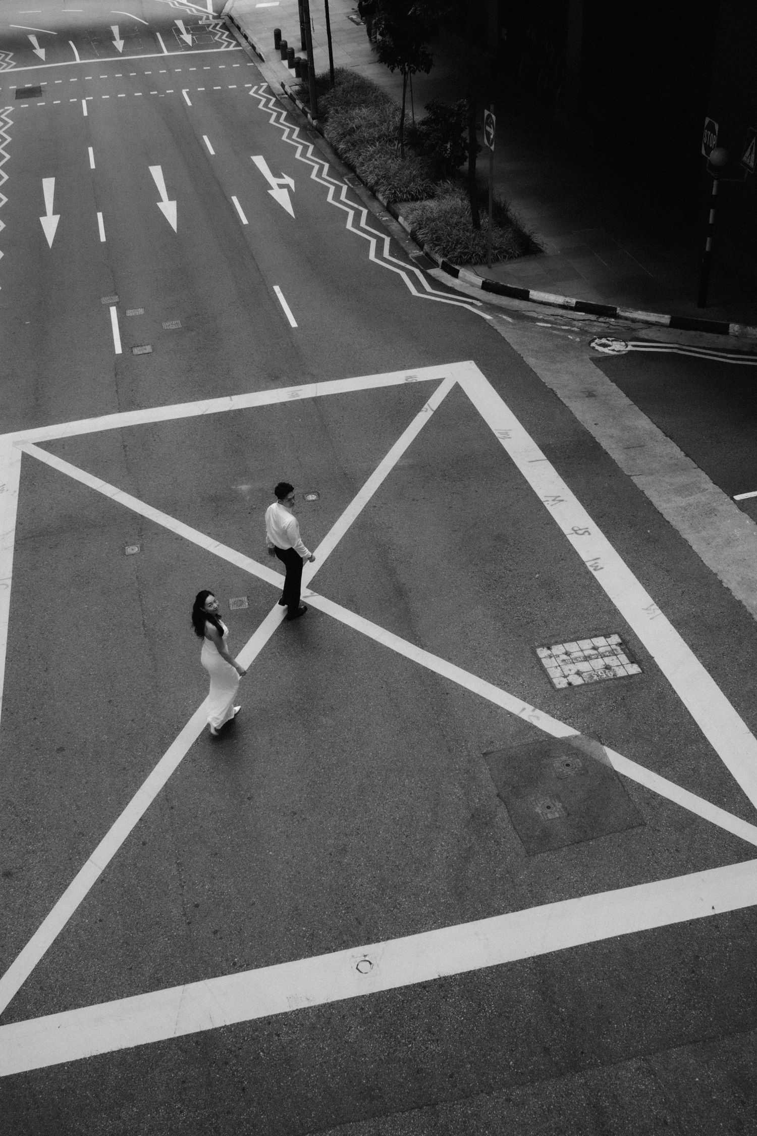 Aerial black and white view of couple standing on geometric road markings at intersection.