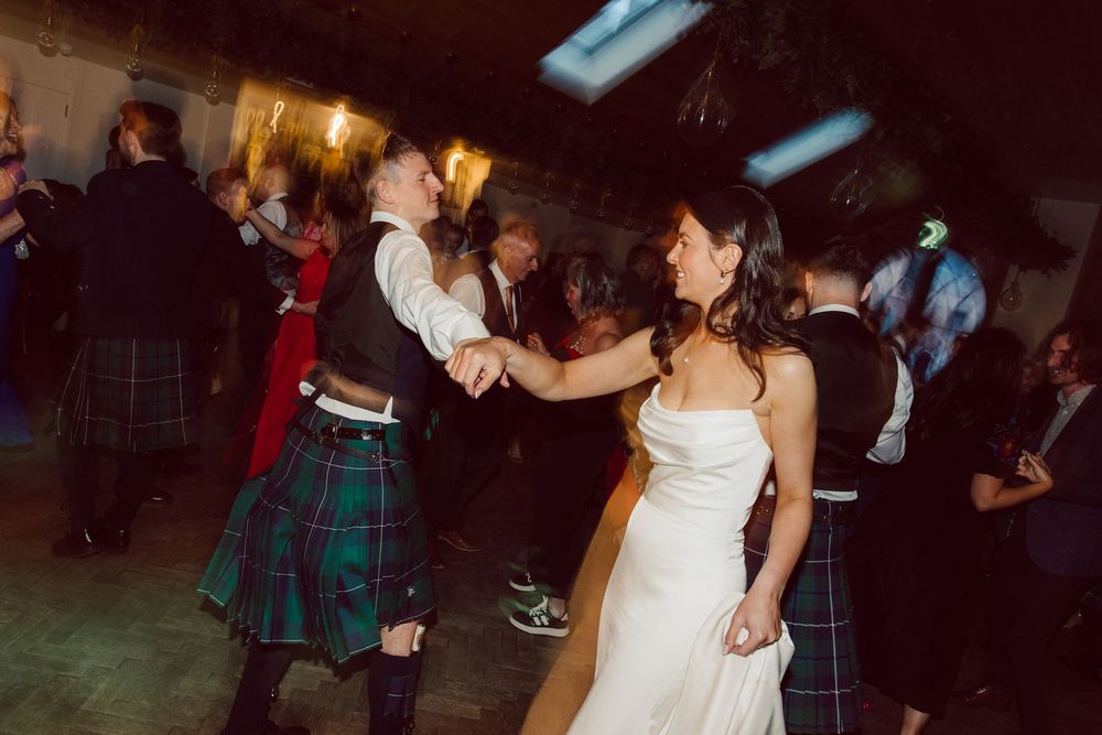 Wedding guests dance together at a dimly lit reception with candlelight and festive atmosphere.