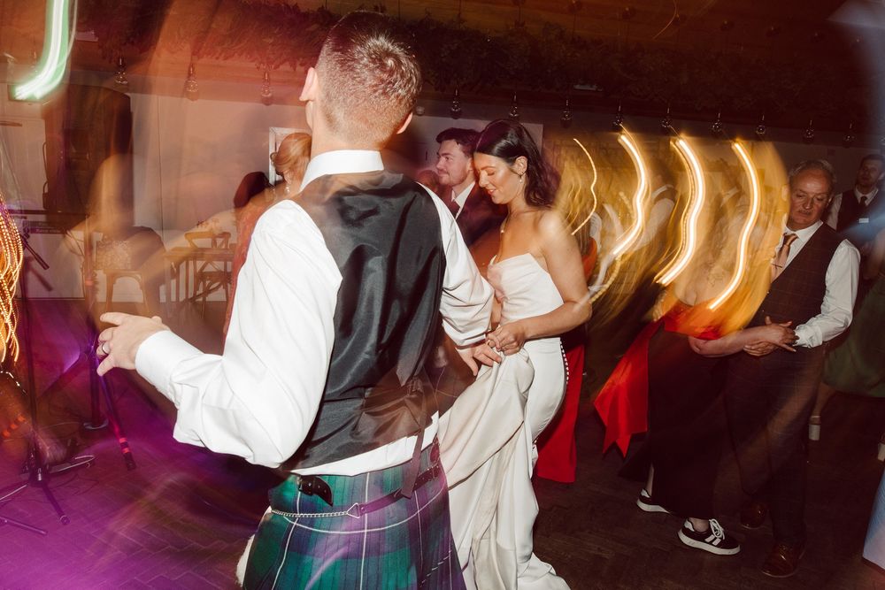 Wedding reception dance floor filled with guests enjoying the celebration in dark lighting.