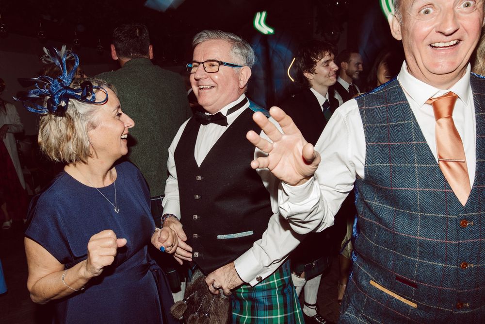 Guests dance and celebrate together at an evening wedding reception with plaid attire visible.
