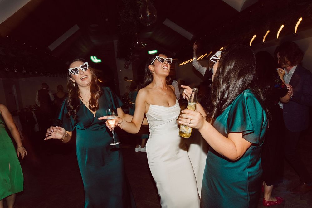 Wedding guests dance and celebrate on a dark dance floor with people wearing formal attire and teal dresses.