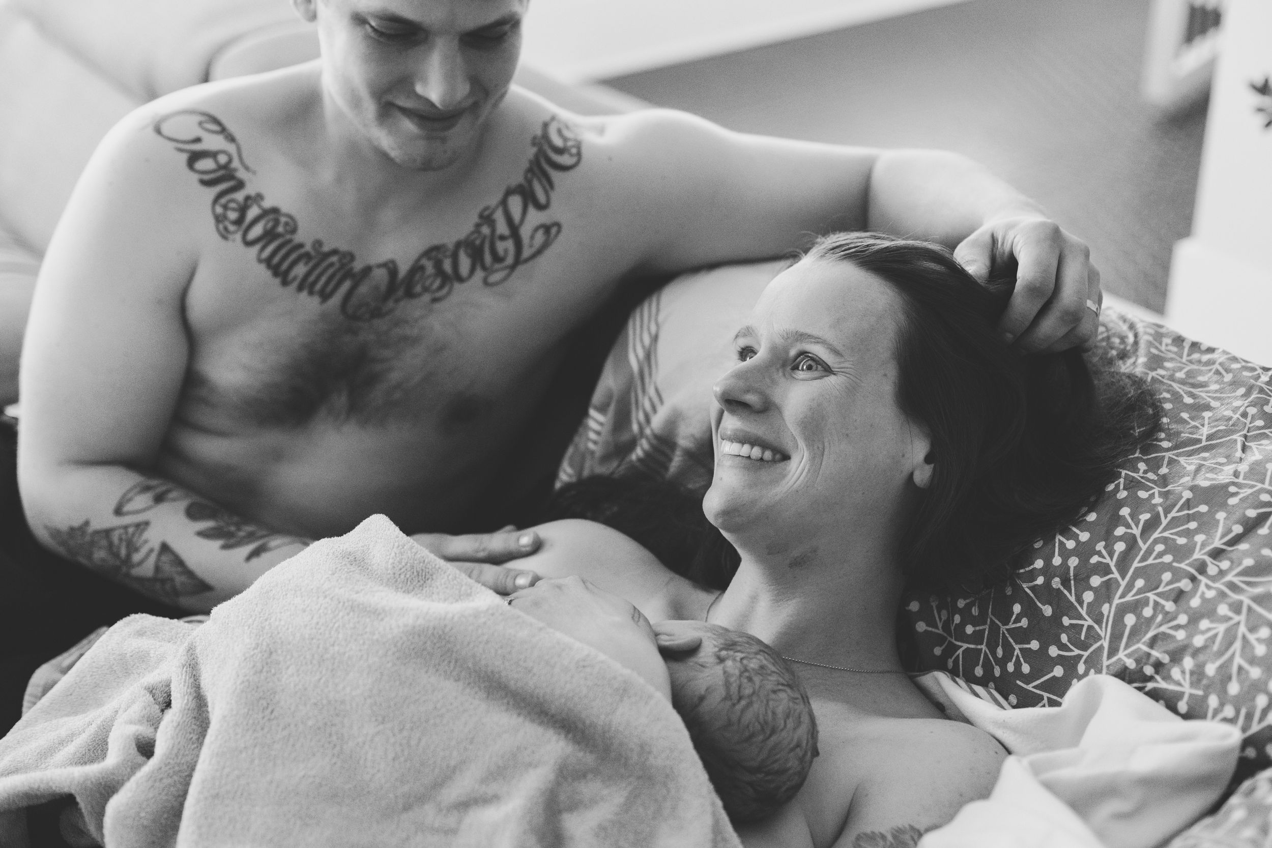 Mom and dad holding newborn baby after home birth in Ottawa. Baby is on mom's chest and mom is smiling.