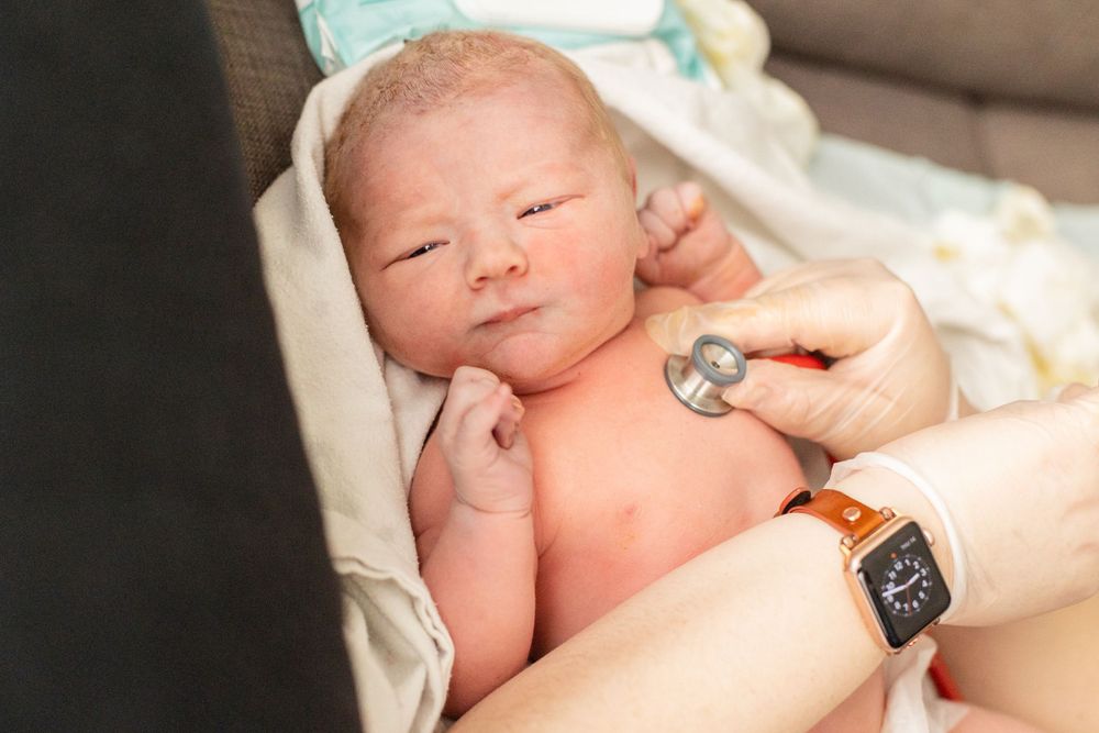 Closeup of newborn baby during midwife health check right after birth at home.