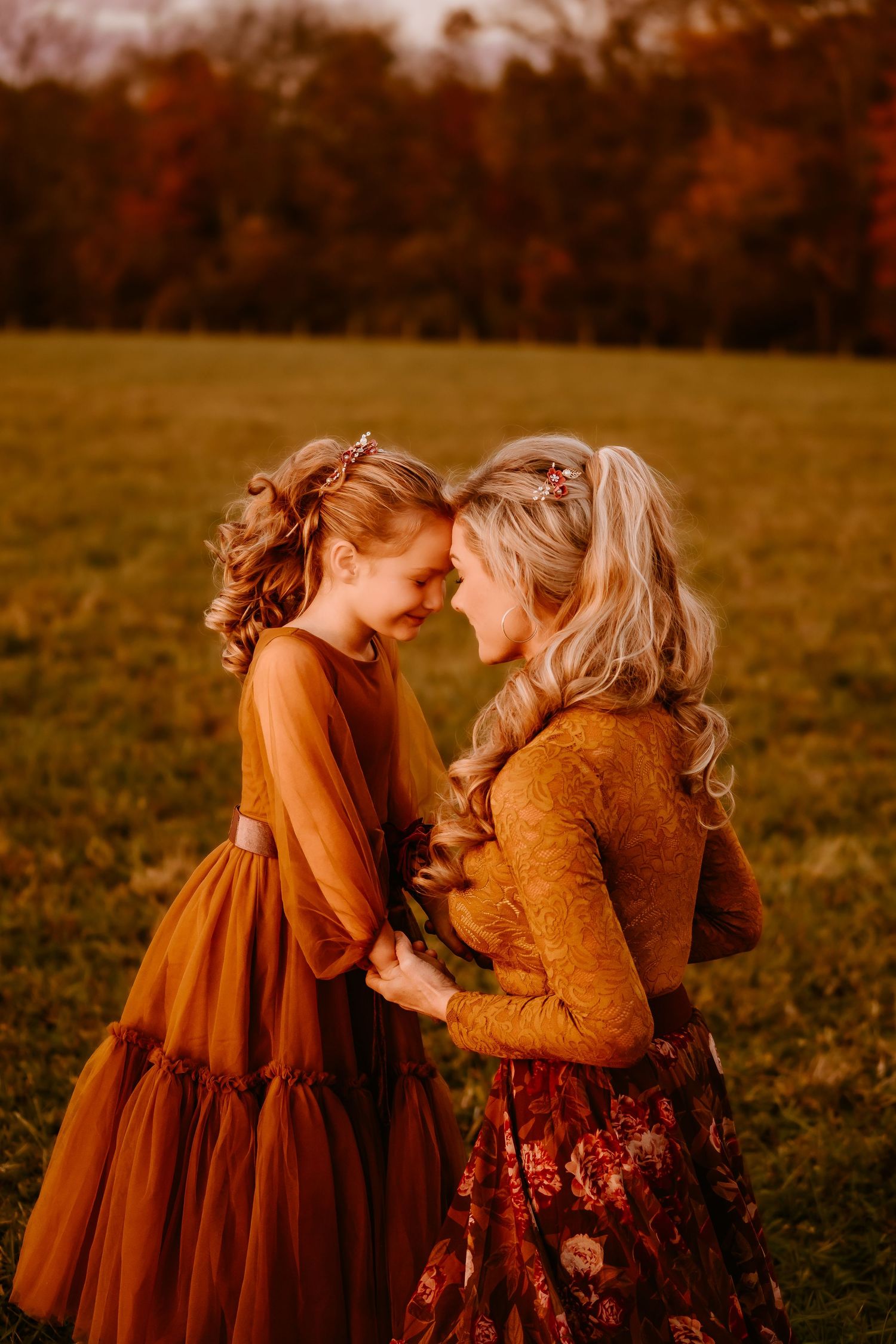 Mother and daughter in matching rust and burgundy fall dresses smiling together in an autumn field.