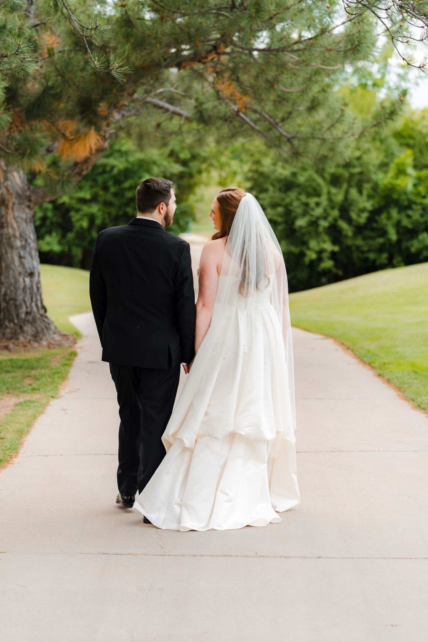 Bride and groom walking hand in hand on a path surrounded by lush greenery on their wedding day.