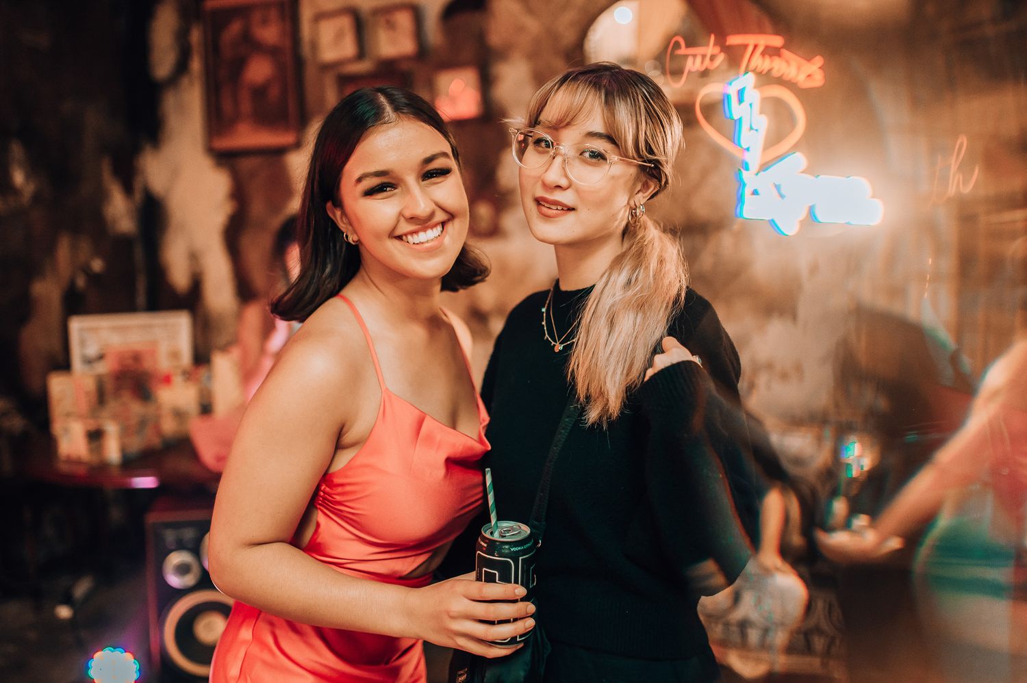 Two friends enjoying drinks and nightlife at a bar with neon lighting.