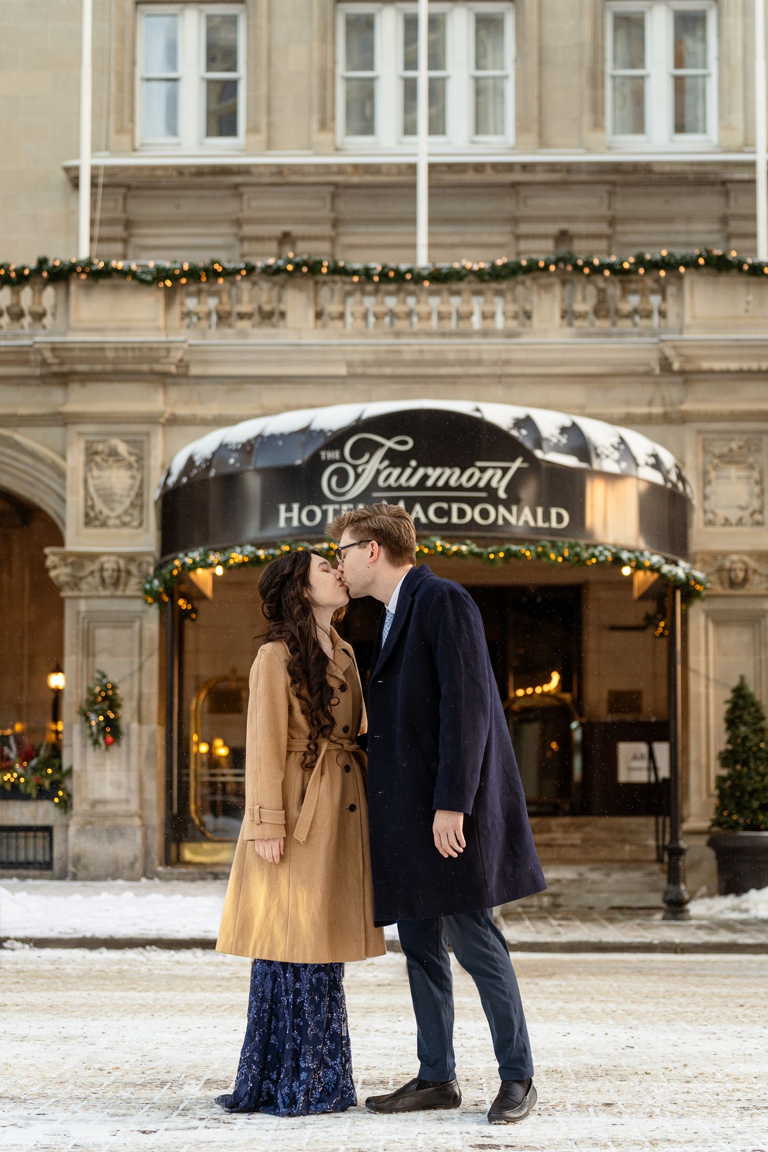 Romantic winter engagement photos at the Fairmont Hotel Macdonald with couple in navy and tan outfits in the snow.