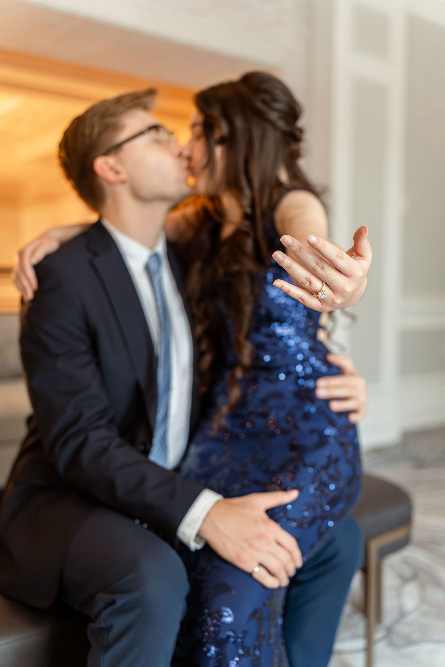 A couple in formal attire share a romantic dance together, with the woman wearing a sparkling navy blue dress.