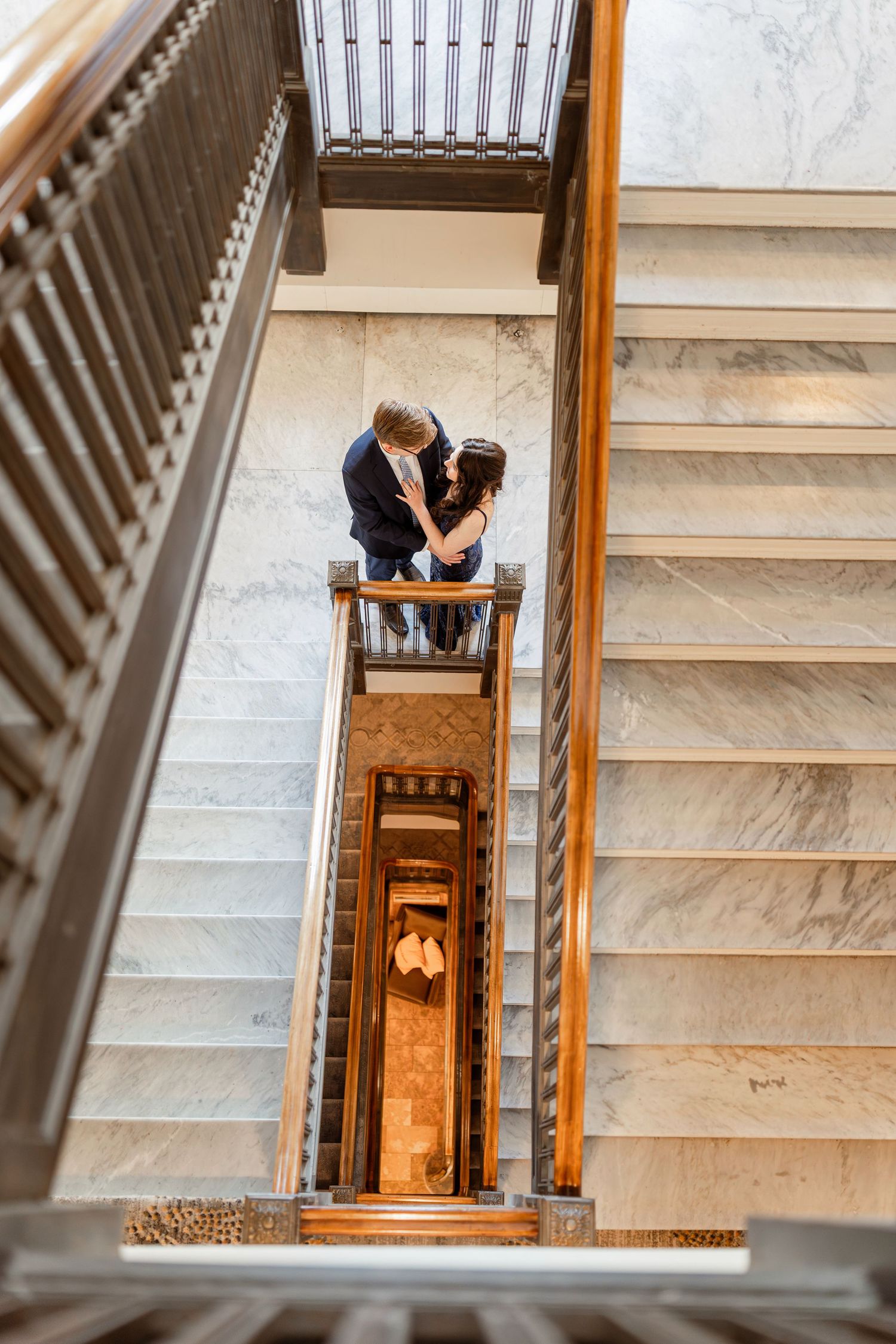 Looking down a grand marble staircase with wooden railings in an elegant building interior.