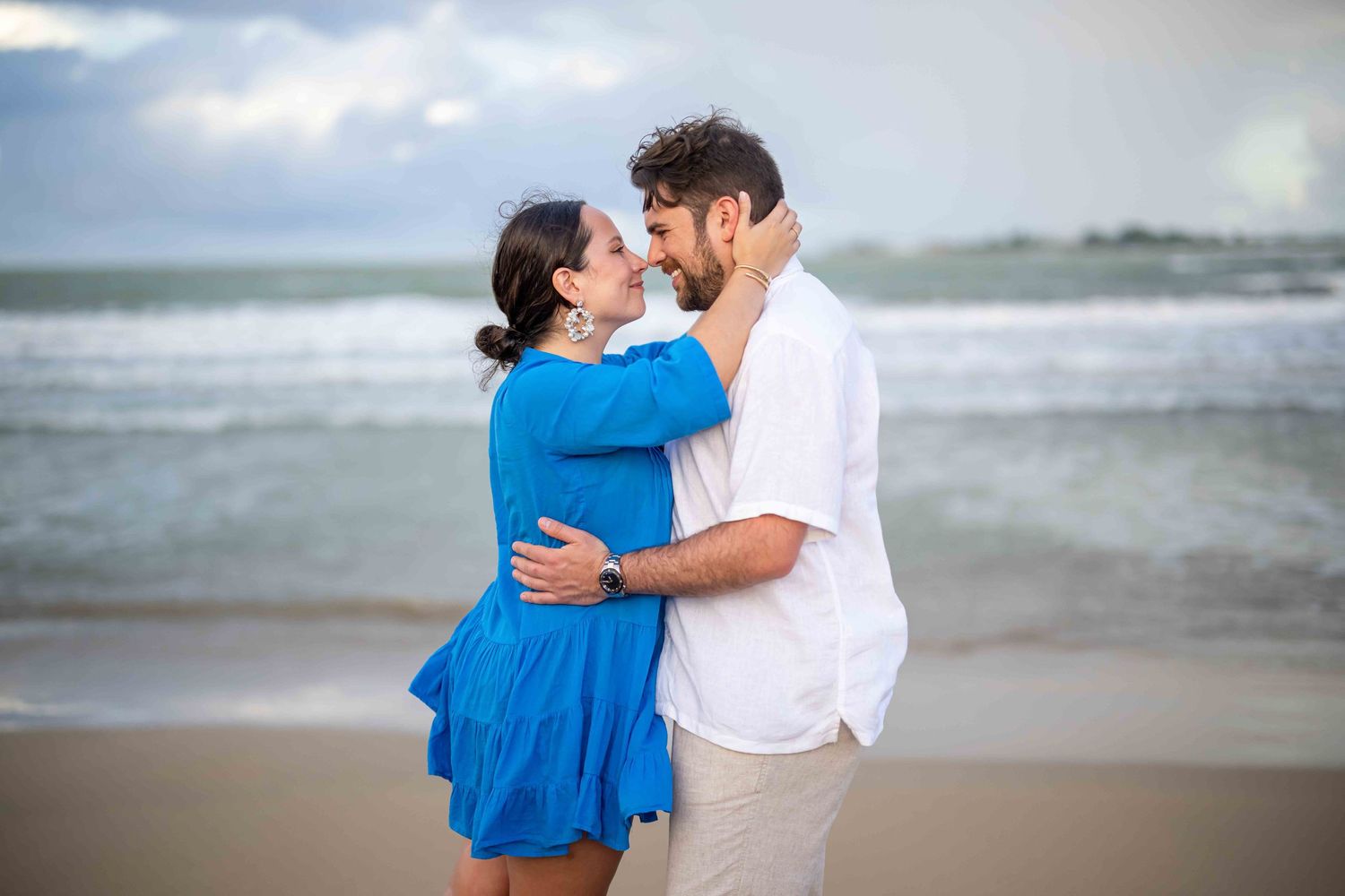 Couple sharing a romantic moment on the beach with ocean waves in the background.