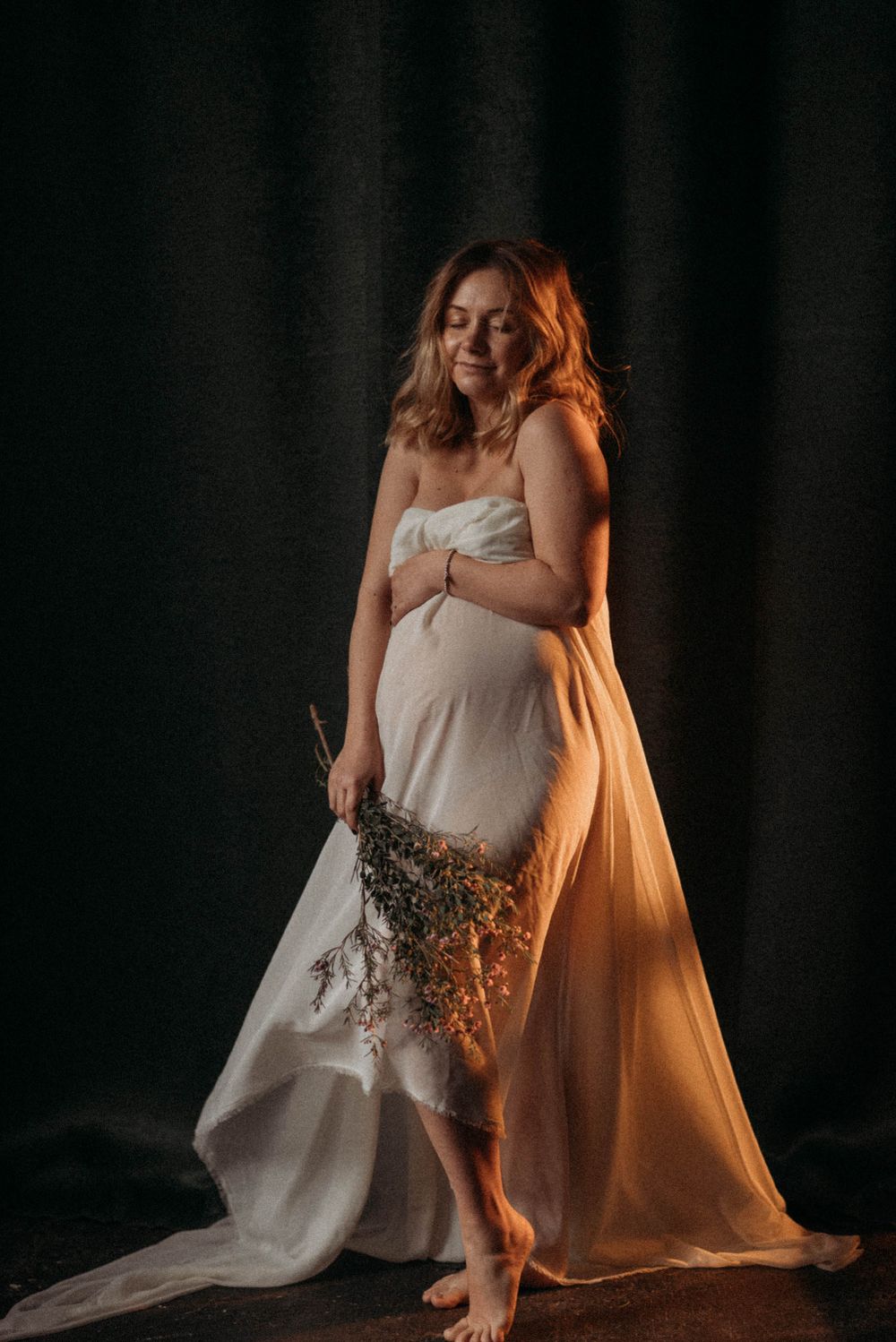 Dramatic portraits in flowing dress with warm lighting against dark background.