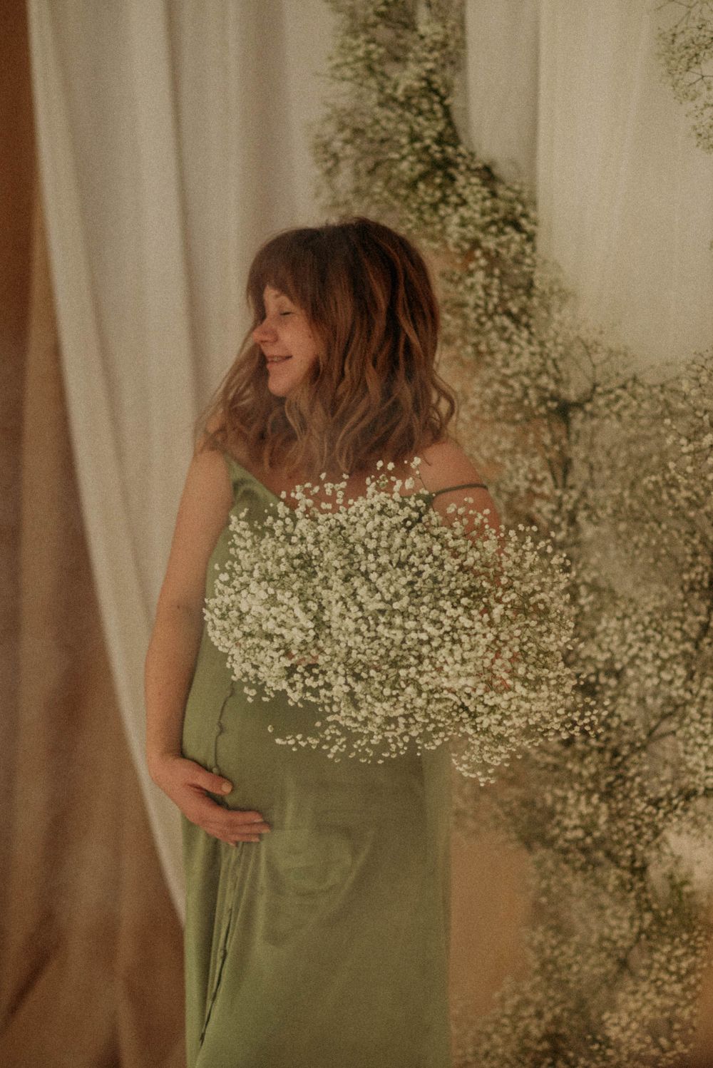 Pregnant woman smiling in a studio, holding her belly with one hand and flowers in the other.