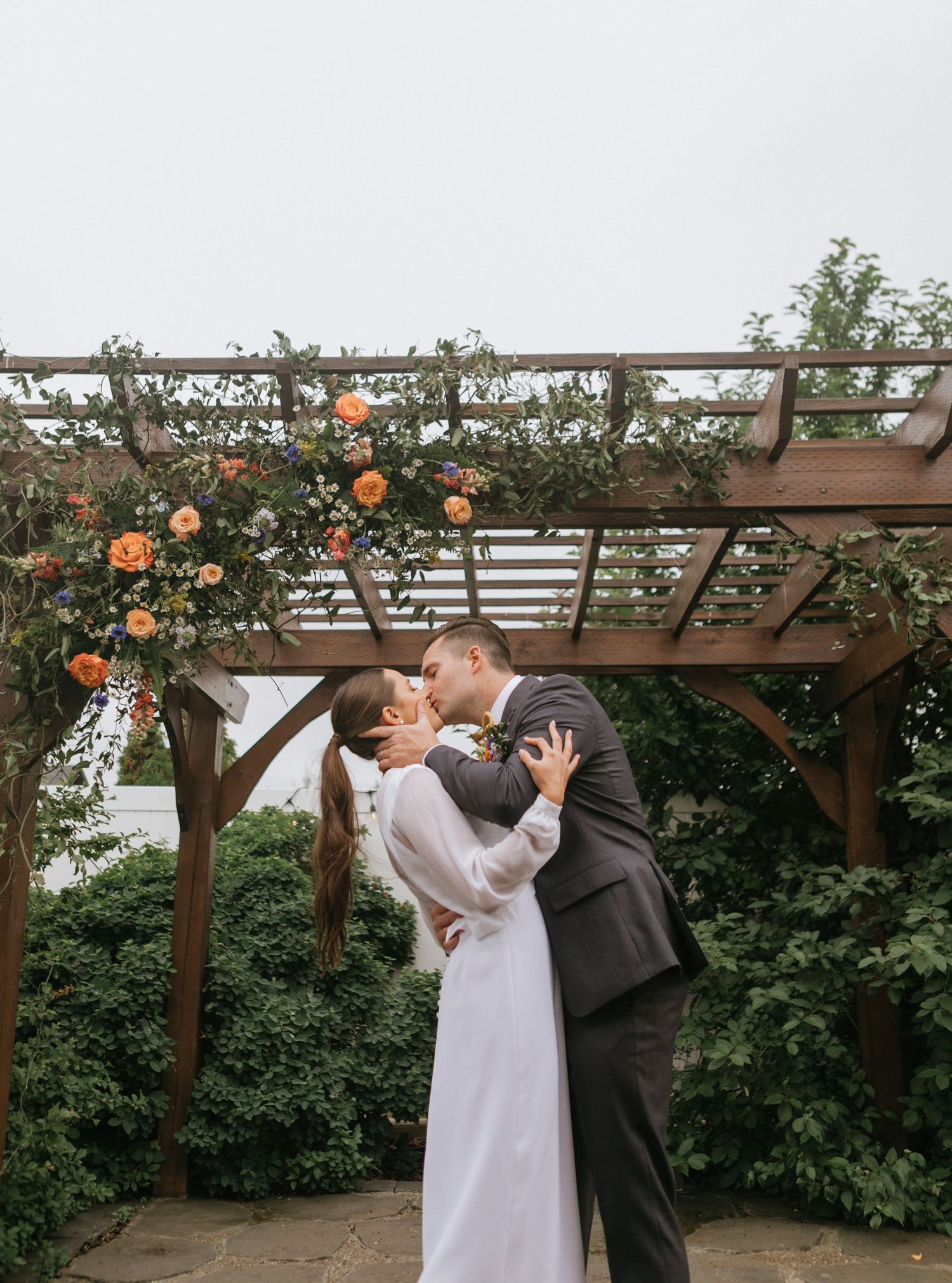 Romantic kiss under wooden pergola decorated with climbing orange roses.