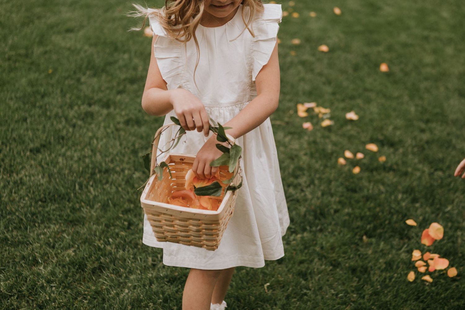 Young child in white dress holding wicker basket during outdoor event.