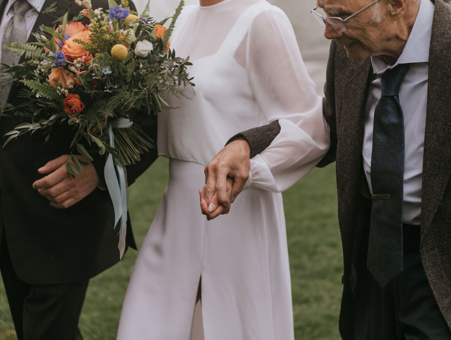 Elegant wedding attire detail with white jumpsuit and colorful bouquet.