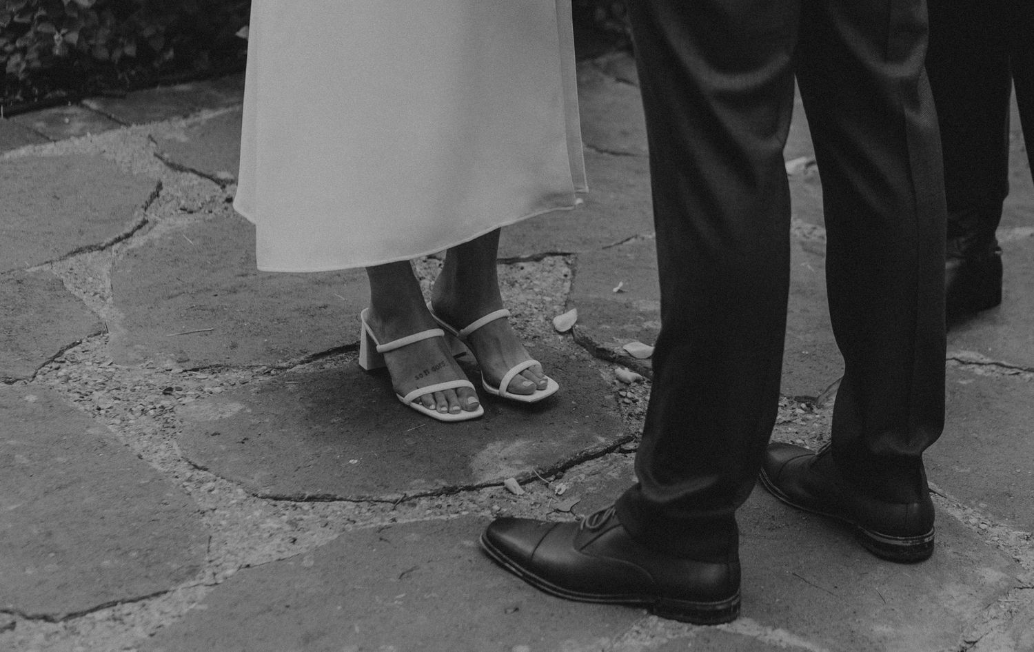 Black and white photograph of formal shoes and dress shoes on stone pavement.