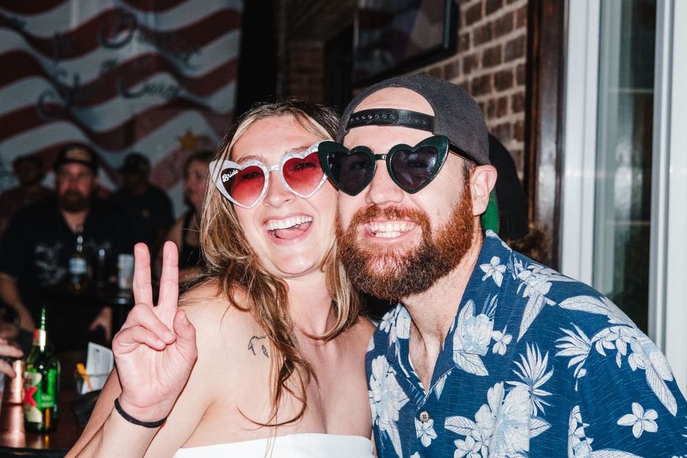 Two people wearing sunglasses and smiling while enjoying a sunny outdoor gathering.
