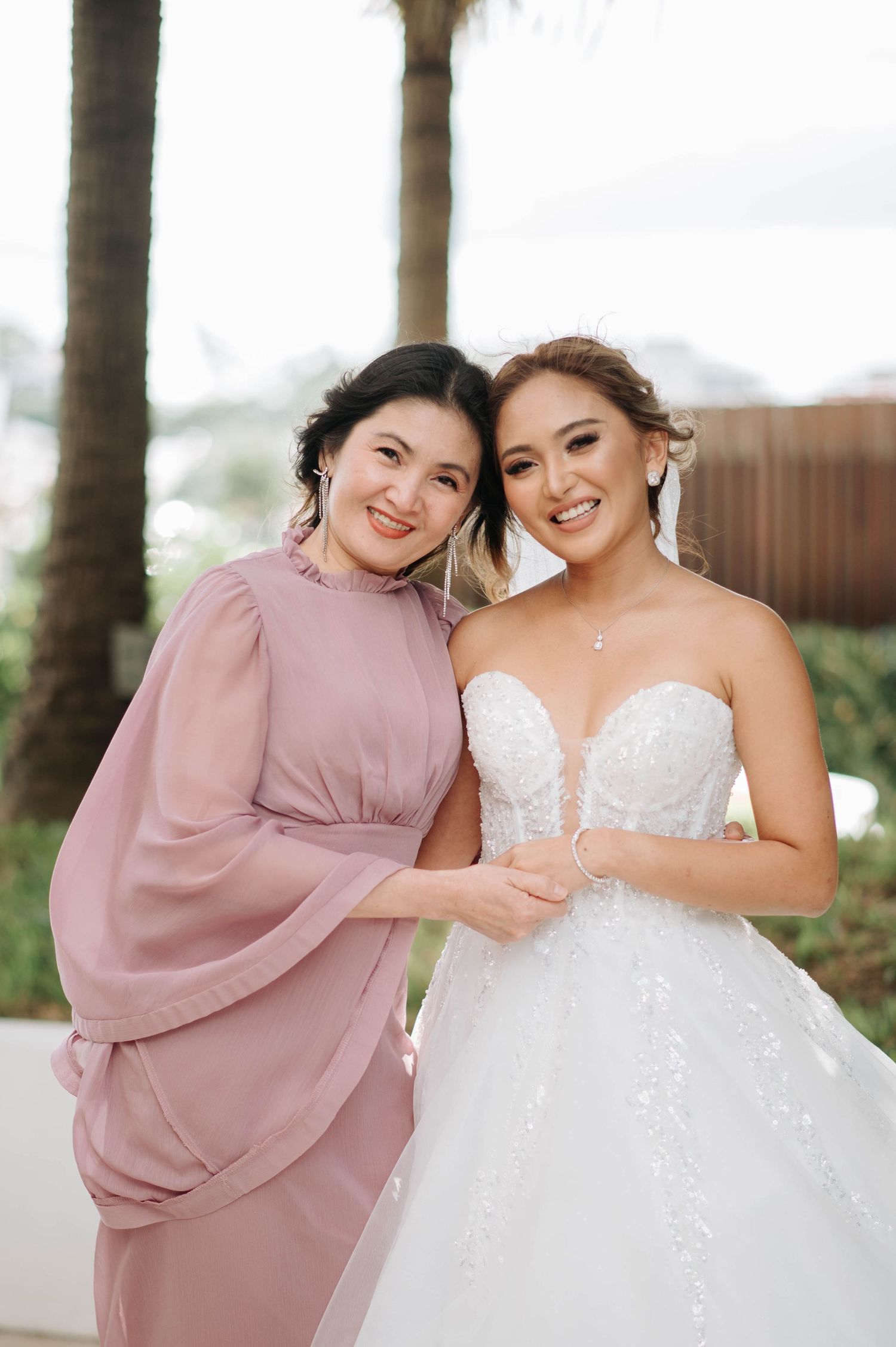 Two people in pink and white formal attire pose together outdoors.