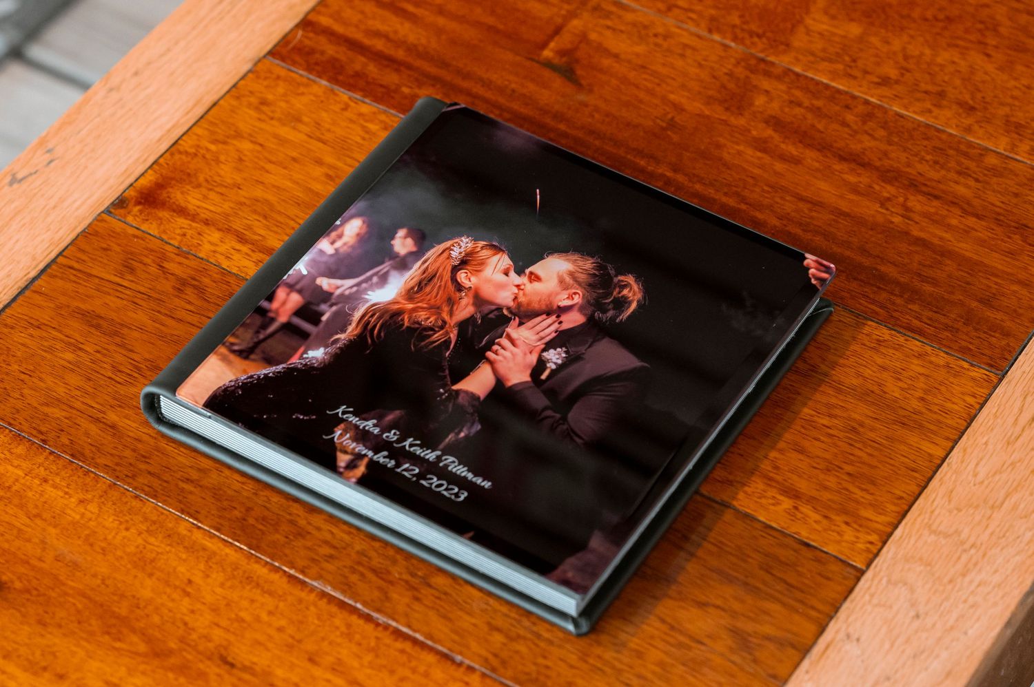 Dark wedding photo album lying on wooden surface with embossed cover design.