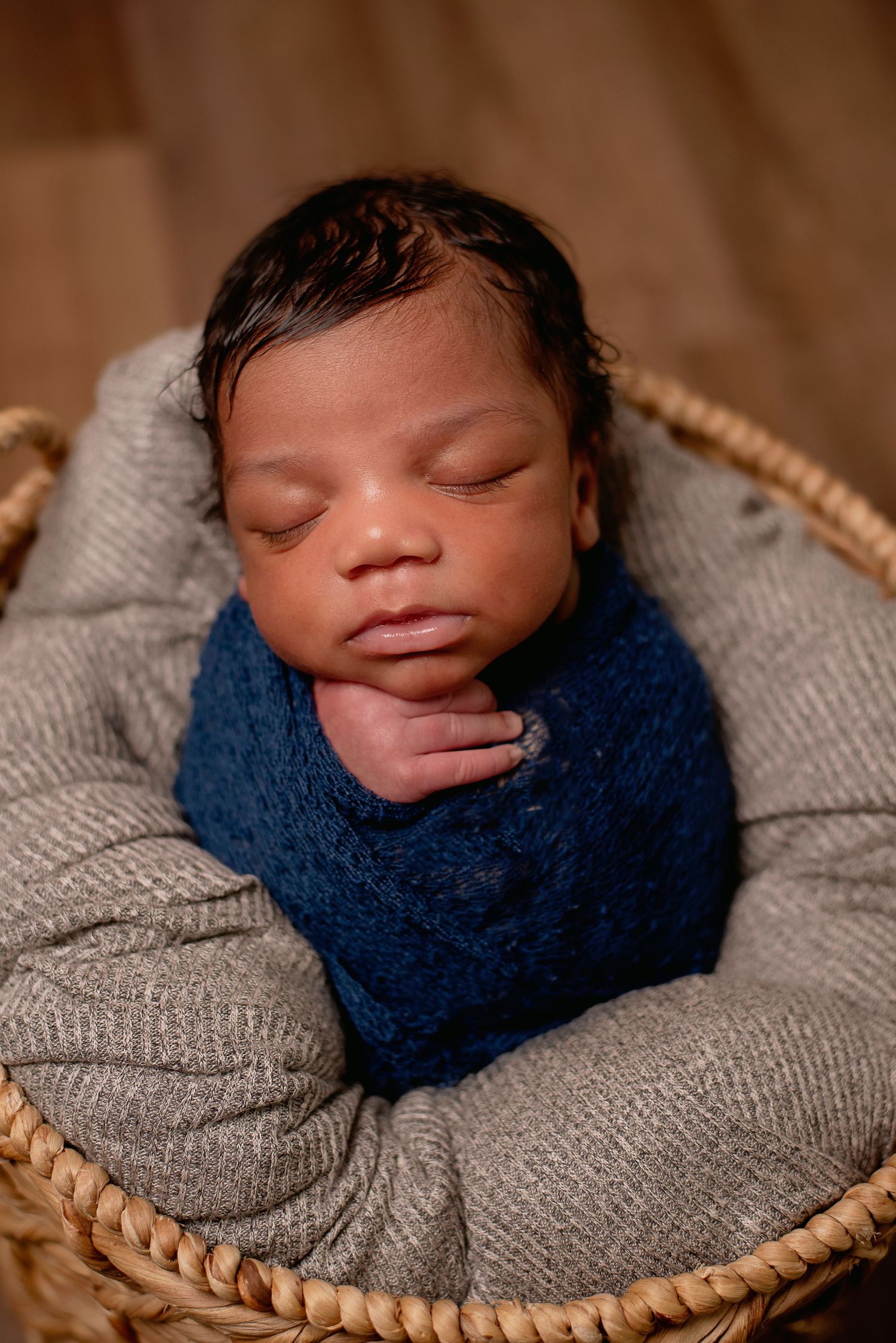 Peaceful sleeping newborn wrapped in blue and grey in woven basket.