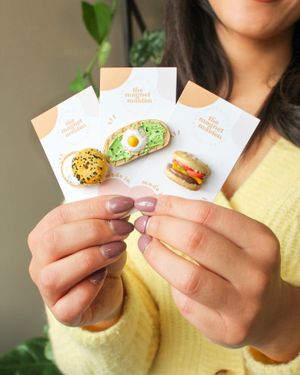 woman holds up three food inspired clay magnets.