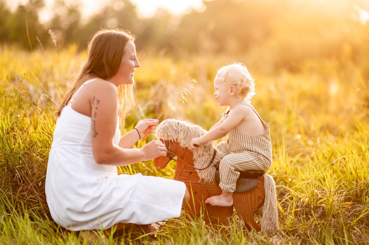 A tender moment shared between mother and baby outdoors in a golden sunlit meadow at sunset.