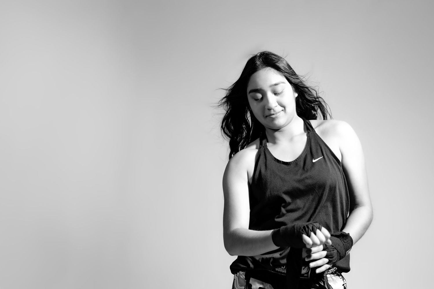 Black and white portrait of a person with long dark hair in a tank top against a plain background, eyes closed in motion.
