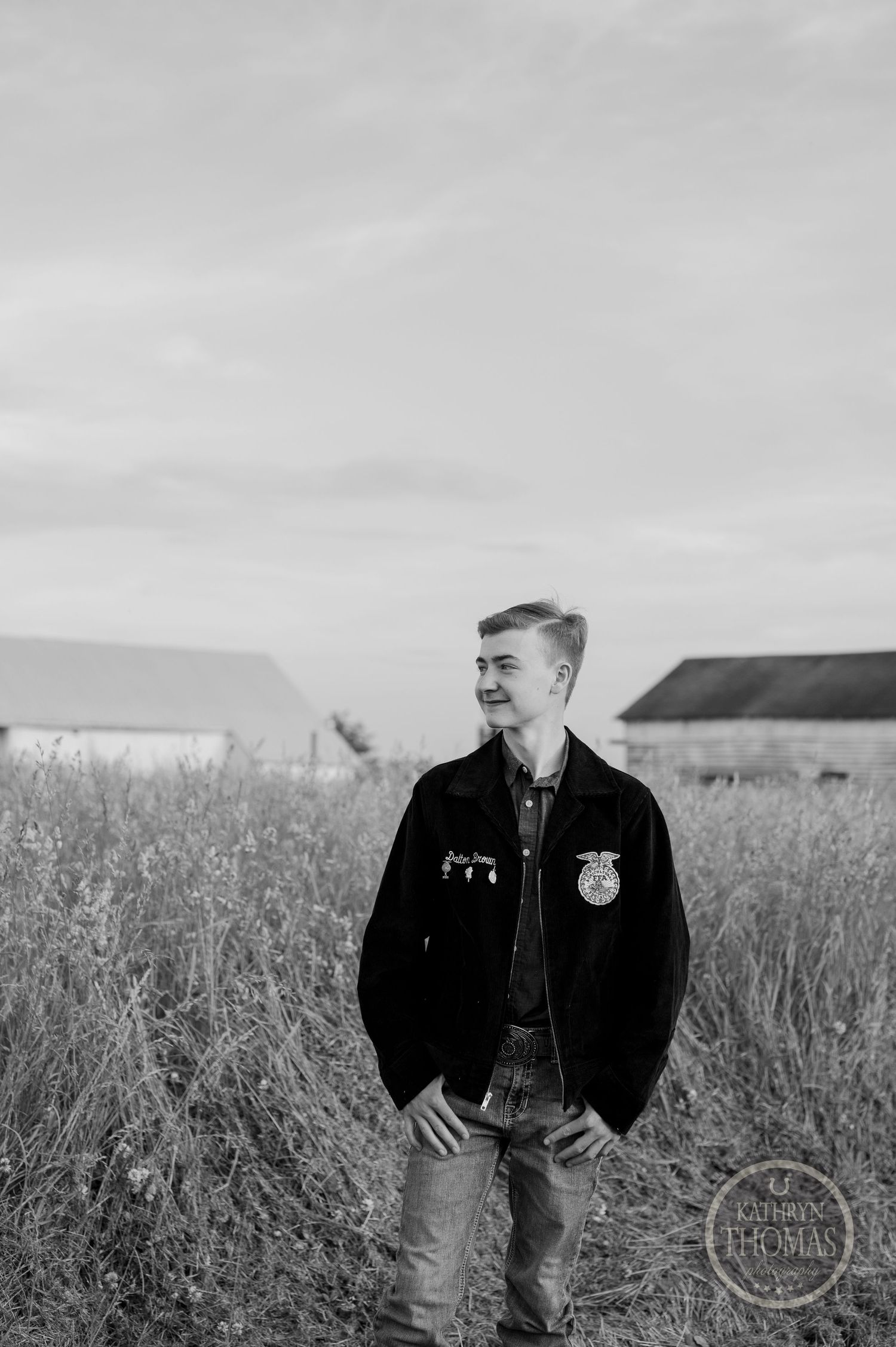 Black and white portrait of student in FFA jacket standing in rural field setting.