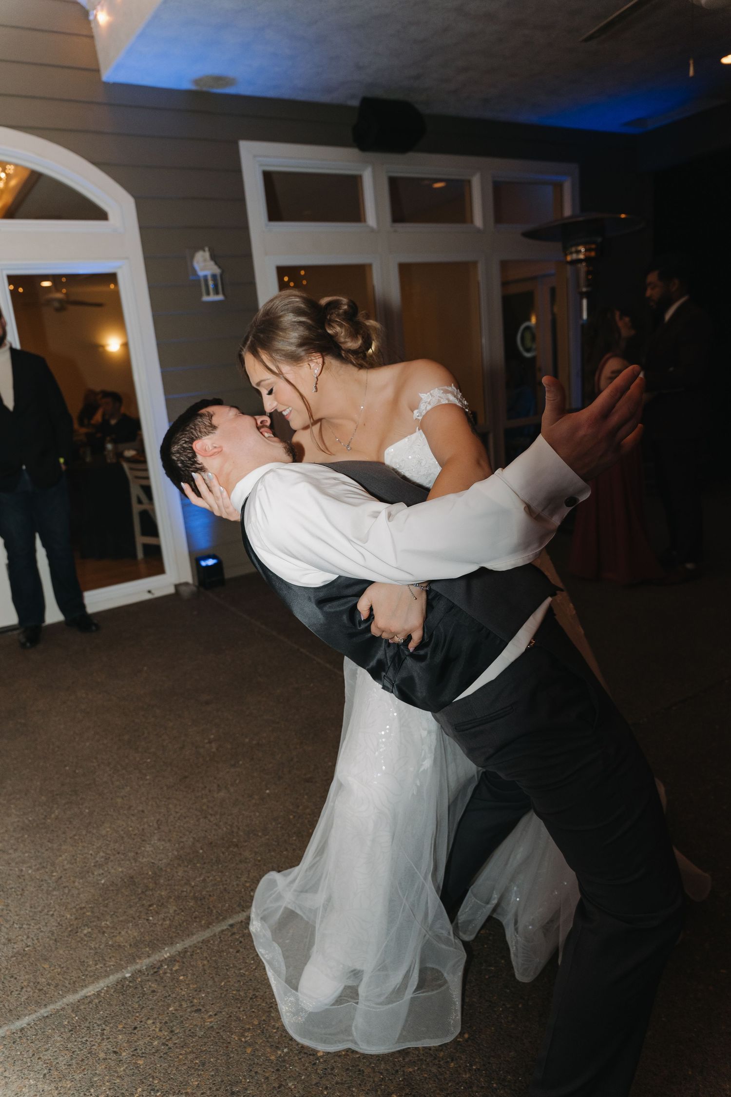 Couple shares romantic dance dip moment at wedding reception with blue lighting in elegant venue.