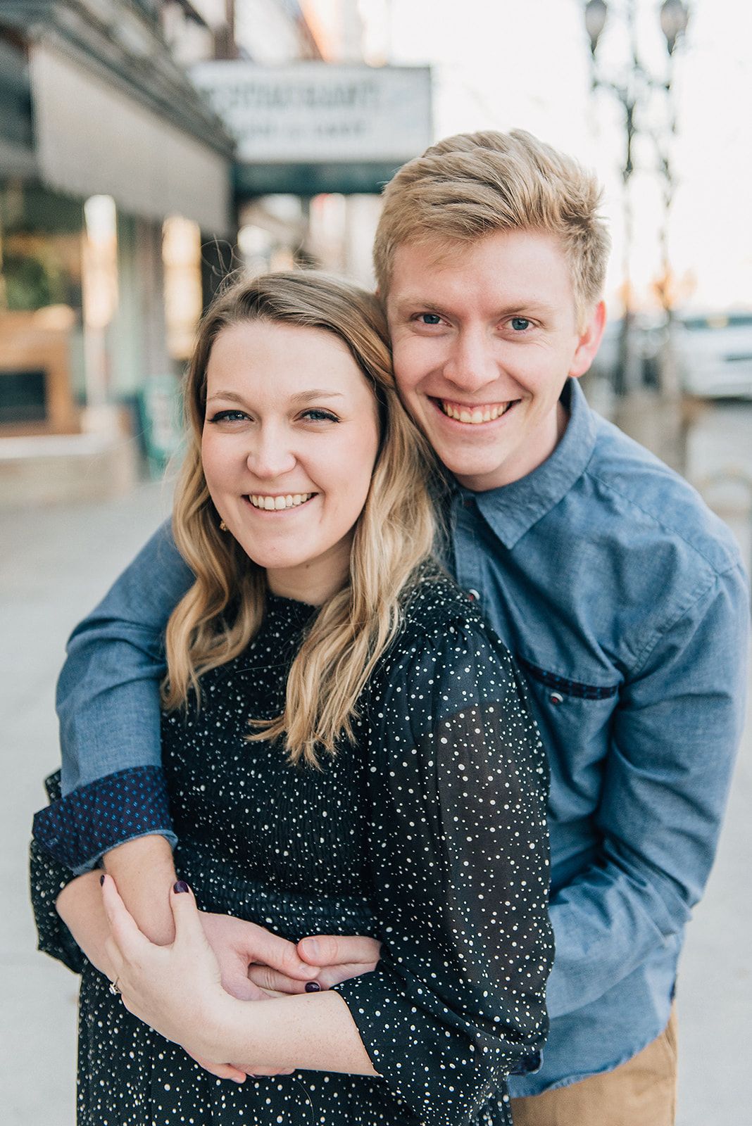 Couple embracing and smiling together outside storefront on urban street.