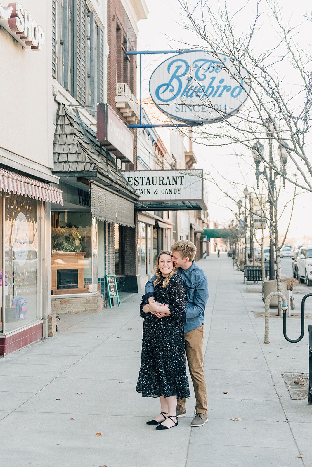 Couple standing together beneath Bluebird restaurant sign on city sidewalk.
